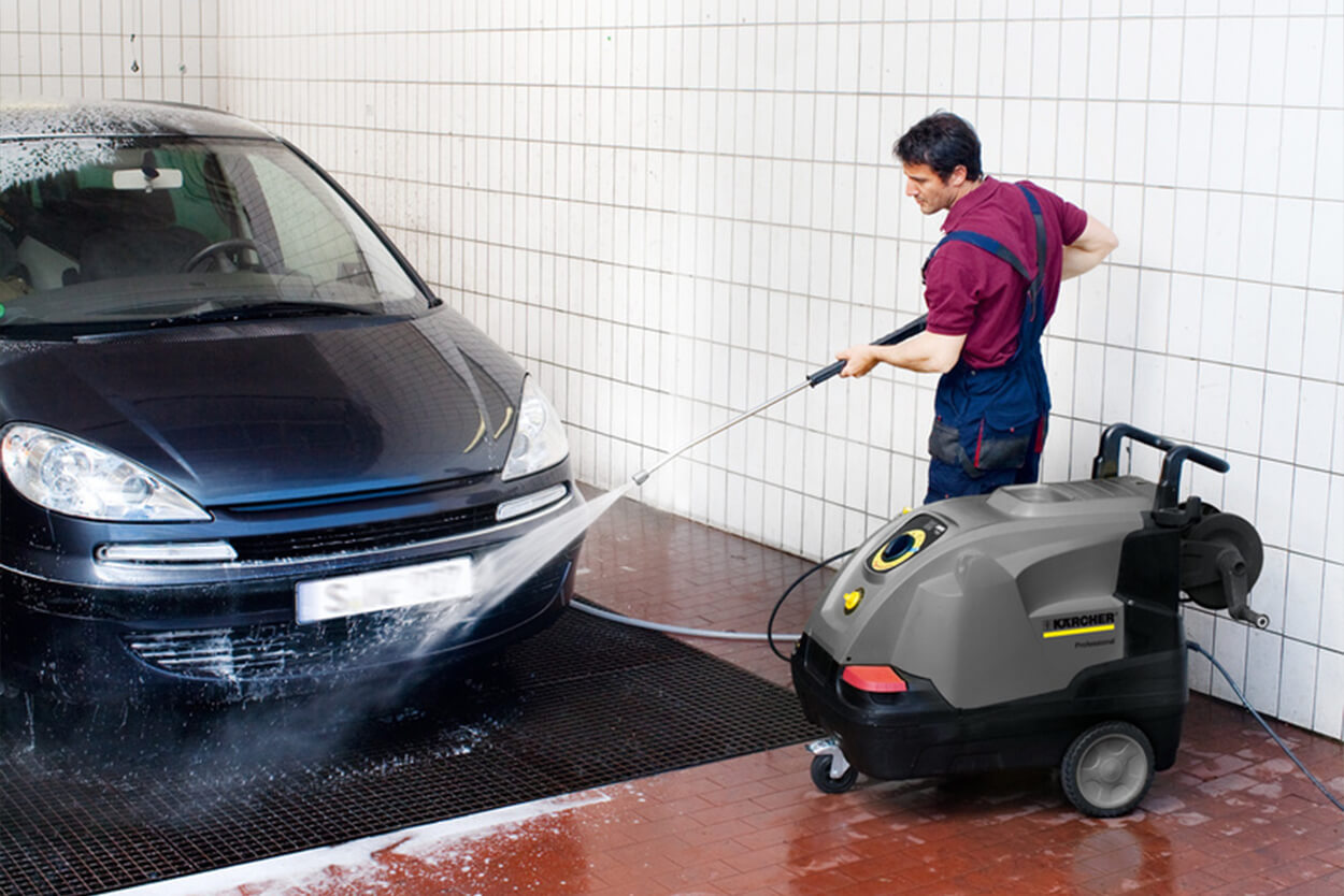A man cleaning a navy car indoors with HDS pressure washer