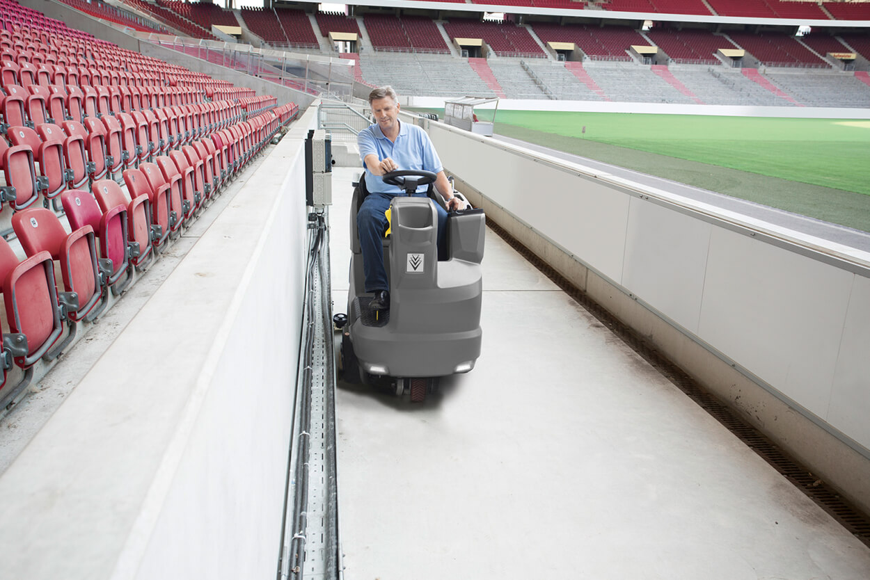 Man riding B 150 R Ride-On Scrubber Dryer in empty sports stadium