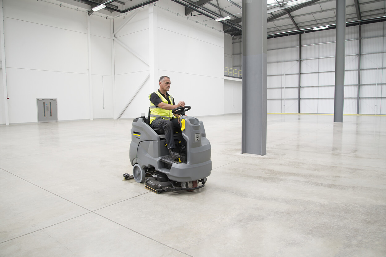 Man riding B 150 R Ride-On Scrubber Dryer in empty warehouse