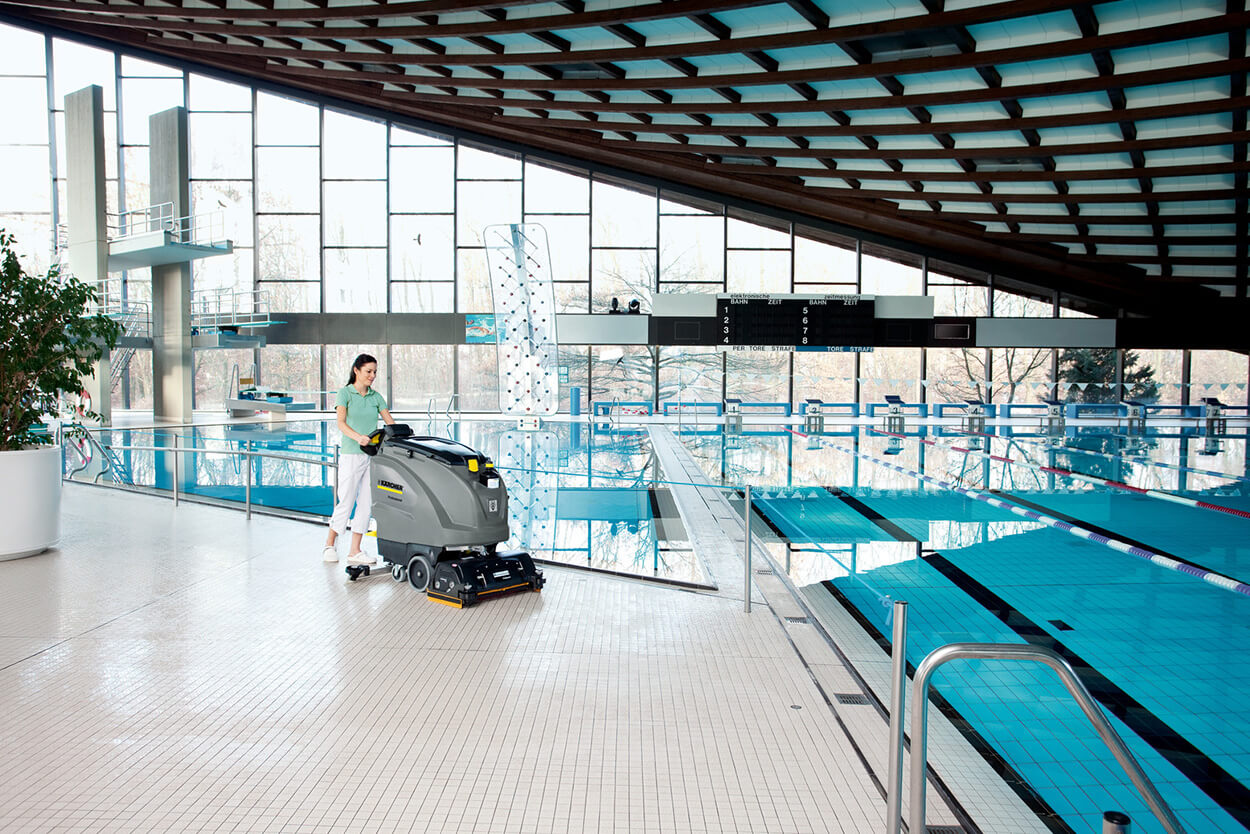 Women operating B 60 W scrubber dryer cleaning machine at empty swimming pool