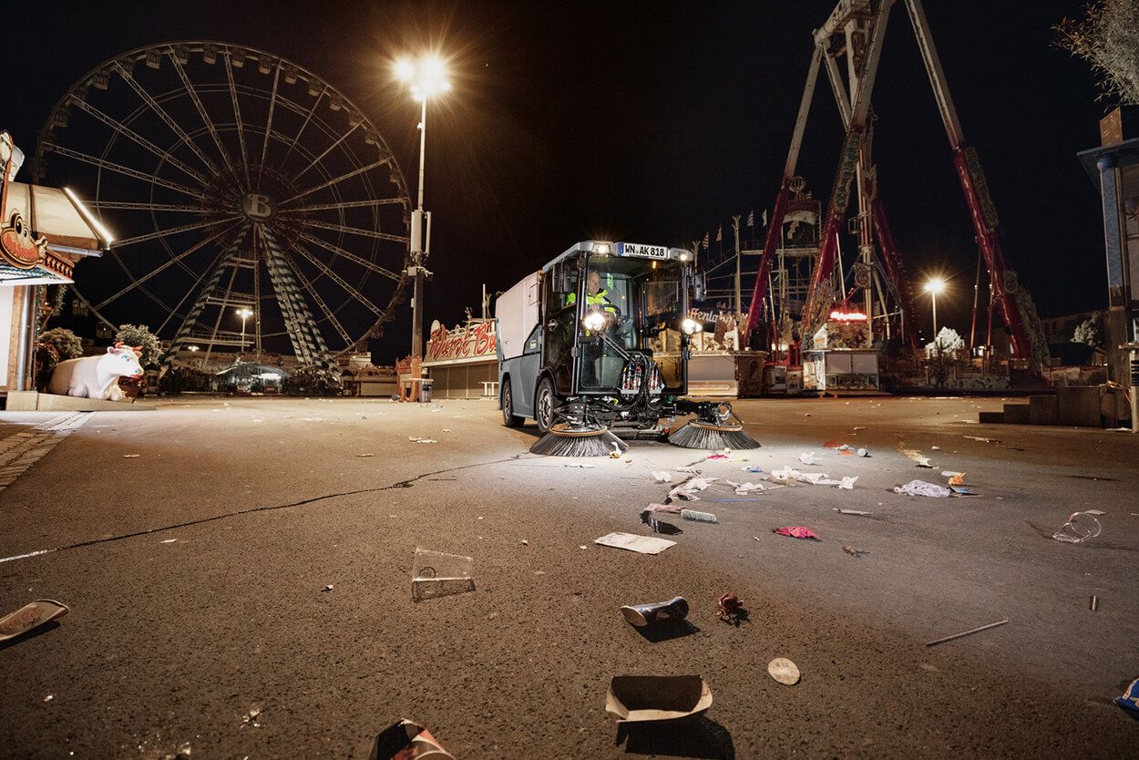 Man using MC 250 Sweeper, clearing up a road near a dark fair